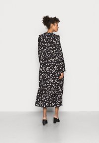 Vestido floral preto com mangas longas, design em camadas e gola franzida. Apresenta um padrão floral leve com cores suaves e uma silhueta fluida.