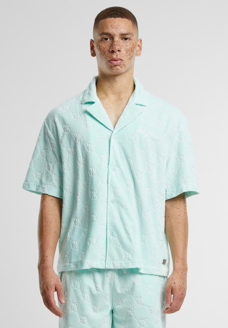 Camisa de manga corta en verde menta con un patrón texturizado de formas entrelazadas, que cuenta con un cierre de botones en la parte delantera y un detalle de logo bordado.