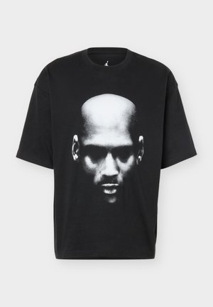 Sort oversized t-shirt med et monokromt close-up grafik af en skaldet mands ansigt placeret i midten foran.