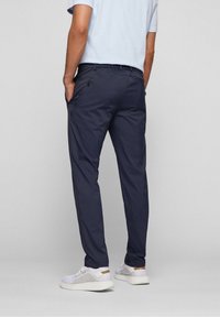 Navy blue athletic pants with a tapered fit, elastic waistband, side pockets, and a smooth texture, paired with white sneakers.