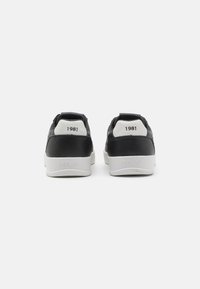 Schwarze Ledersneaker mit weißen Akzenten, ausgestattet mit einem erhöhten Absatz, geprägtem "REPLAY"-Logo und "1981"-Aufdruck auf den Fersenlaschen.