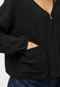 Cardigan zip-up nero realizzato in tessuto testurizzato, con scollatura a V, maniche lunghe e due tasche frontali.