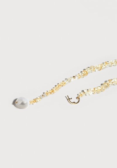 Collier délicat avec de petites perles jaunes translucides, un pendentif en grosse perle blanche, et un fermoir à crochet en or sur un fond clair.