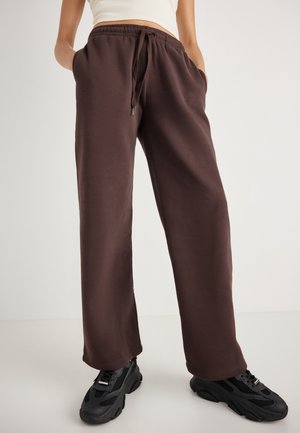 Beige Sweatpants mit entspanntem Schnitt, elastischem Bund mit Kordelzug, Seitentaschen und kombiniert mit schwarzen strukturierten Sneakern.