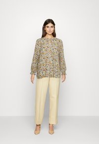 Blusa floral de mangas longas, tecido leve, estampa multicolorida, decote redondo com detalhe em fenda, combinada com calças beje ajustadas.