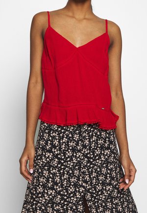 Femme portant un haut rouge sans manches à volants associé à une jupe noire fleurie avec de petites fleurs blanches.