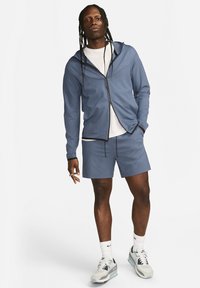 Blue athletic zip-up hoodie over a white t-shirt, paired with blue shorts. Light, smooth fabric with contrasting black accents and drawstrings.