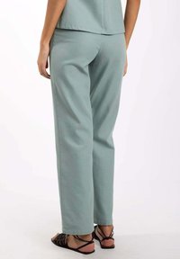 Pantalon vert menthe clair en coupe décontractée, fabriqué à partir d'un tissu doux avec une texture lisse. Dispose de poches latérales ; associé à des sandales noires à lanières.
