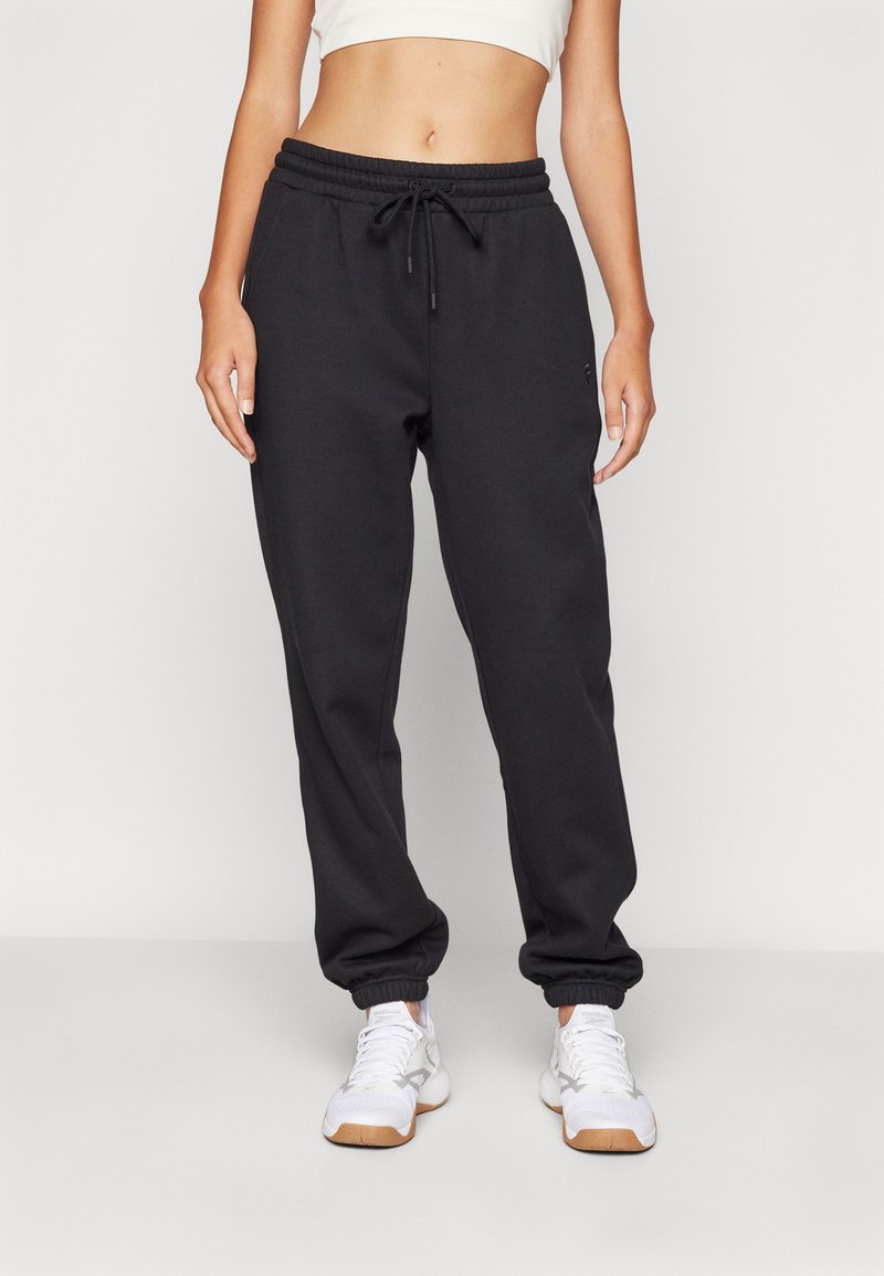 Svarte joggebukser med elastisk midje og snøring, smalnet ben og sidelommer, kombinert med hvite treningsko.
