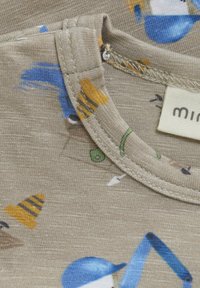 Beige Baumwollhemd mit rundem Halsausschnitt, das mit blauen, gelben und grünen Baustellenmotiven verziert ist. Weiche Textur, sichtbare Nähte.