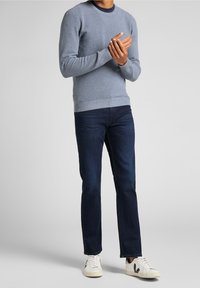 Grå stickad tröja, rund halsringning, långa ärmar; tillsammans med mörkblå jeans och vita sneakers med svarta detaljer.