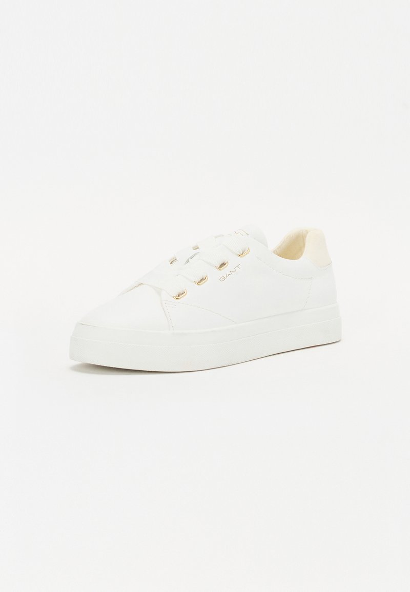 Sneaker blanche avec un extérieur en cuir lisse, bout rond, œillets dorés et semelle en caoutchouc blanc texturé. Branding minimal sur le côté.
