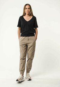 Zwarte katoenen v-hals t-shirt gecombineerd met lichtbeige joggingsbroek met elastische tailleband en beige sneakers met zwarte en grijze accenten.