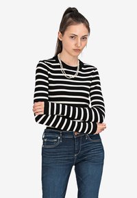 Czarny i biały sweter w paski z długim rękawem, o prążkowanej fakturze, zestawiony z ciemnoniebieskimi dżinsami. Posiada okrągły dekolt i dopasowane rękawy.
