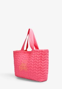 Borsa a tote trapuntata rosa con due manici in tessuto, caratterizzata da un design di teschio e ossa incrociate giallo sulla parte anteriore. Texture morbida e imbottita.