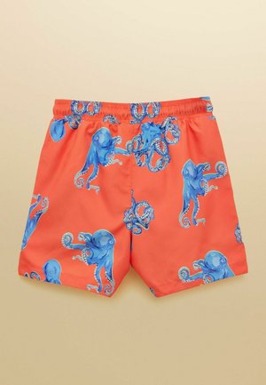 Jasnopomarańczowe kąpielówki z wzorem niebieskich ośmiornic na całej powierzchni i elastycznym paskiem w talii na beżowym tle.