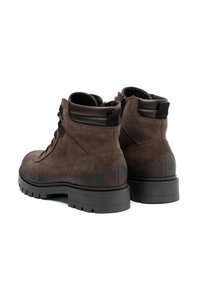 Botas de tobillo de ante marrón con suelas de goma, cordones en la parte frontal, ojales metálicos y detalles acolchados en el tobillo; en la parte posterior tienen una lengüeta para facilitar el uso.