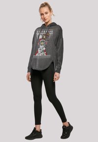 Szürke kapucnis pulóver, mesefigurás nyomattal, fehér és piros kiegészítőkkel, hosszú ujjaival és ívelt alsó résszel, fekete leggings-szel párosítva.