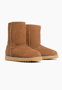 Botas de tobillo de ante de color beige con punta redondeada y una superficie texturizada. Presentan una suela de goma con estrías y acentos de costura decorativa.