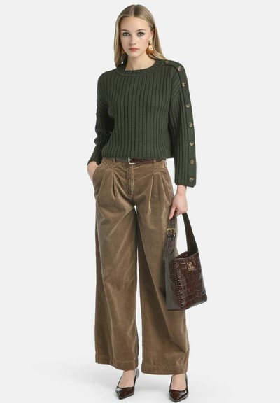 Pulover tricotat ribat de culoare verde închis, cu accente de nasturi pe mânecă, asortat cu pantaloni din catifea lățită de culoare maronie și o geantă lucioasă de culoare maronie.