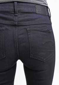 Mörka jeans i denim med en något blekt finish, som visar en slät textur, två bakfickor med böjd söm och en läderlogotyp.