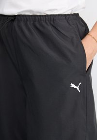 Sorte treningsbukser med elastisk midje, sidelommer, og en hvit Puma-logo. Stoffet ser ut til å være lett og glatt.
