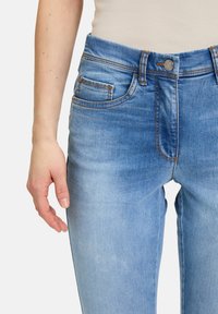 Lichtblauwe denim jeans met een licht vervaagde afwerking, vijf zakken ontwerp, oranje stiksels en een metalen knoopdetail bij de taille.