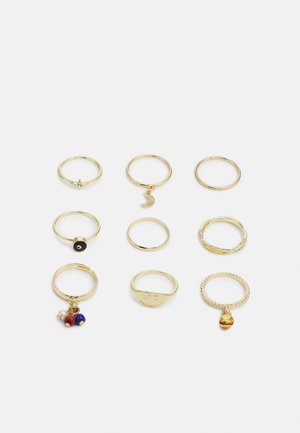 Conjunto de nove anéis dourados com designs variados. Inclui anéis com Charms, texturas e diferentes formas, incluindo lisos e padrões.