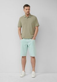 Polo shirt olive clair avec une texture douce et un col à trois boutons, associé à un short vert menthe et des baskets blanches, coupe décontractée.