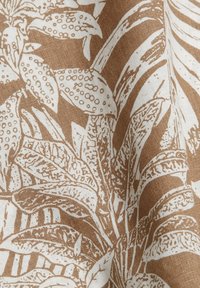 Tissu marron et blanc avec des motifs détaillés de feuilles et plantes tropicales, montrant la texture et les plis.