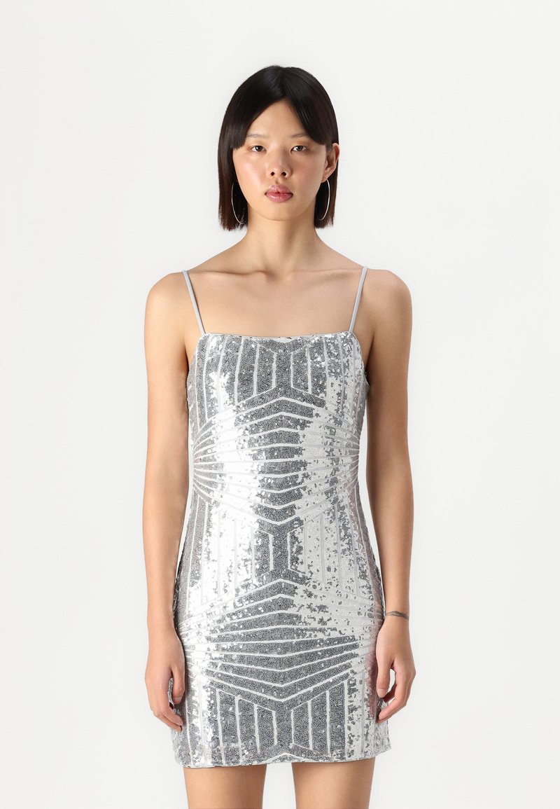Silver sequin mini dress with thin straps, featuring a geometric pattern and fitted shape, reflecting light with a shiny texture.