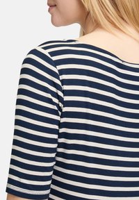 Koszulka w paski w kolorze granatowym i kremowym, z okrągłym dekoltem i krótkimi rękawami, wykonana z miękkiego materiału, o luźnym kroju i widocznych szwach.