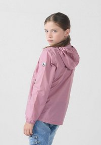 Roze waterdichte jas met capuchon, elastische manchetten en logopatch op de mouw. G gedragen met blauwe spijkerbroek, met een casual pasvorm.