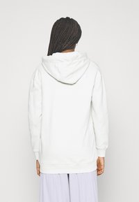 Sudadera blanca con capucha amplia, material de algodón y puños acanalados. Cuenta con un detalle de logo en la parte superior de la espalda y un ajuste holgado.