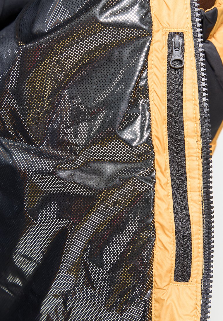 Tela negra perforada con un acabado brillante, realzada por un acento amarillo y un cierre de cremallera en el lateral, que ofrece un detalle de diseño texturizado.