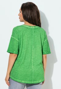 Grünes oversized T-Shirt mit kurzen Ärmeln, aus weichem Stoff gefertigt. Verfügt über einen runden Halsausschnitt und einen leicht geschwungenen Saum.