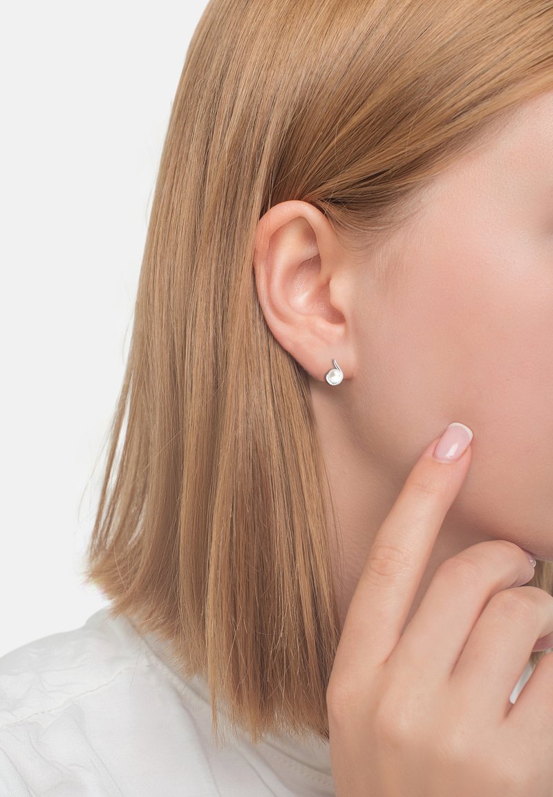 Silverstuds i form av en dropp, med slät yta och polerad finish. Kort, rak blond hår ramar in örat.