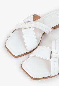 Hvide slidesandaler med firkantet tådesign, krydsrem med metalspænde, flad beige sål og synlige syninger.