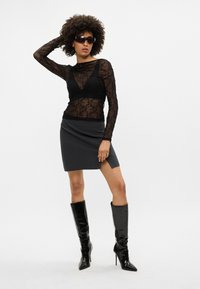 Čierny čipkovaný top s dlhým rukávom preložený cez čierny bralet, skombinovaný so šedou mini sukňou a čiernymi čižmami na vysokom opätku po kolená.