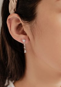 Pendientes de gota plateados con acentos de piedras transparentes, que incluyen formas triangulares y en forma de lágrima, con un diseño de cadena delicada.