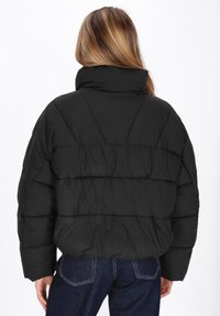 Giacca a vento nera con collare alto, caratterizzata da un design a quadri e cuciture visibili sulla schiena.