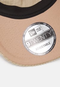 Bežna kapa s crnim detaljima, podesivog fit. Ima teksturiranu površinu tkanine i okruglu oznaku s logom označenom "9TWENTY ADJUSTABLE."