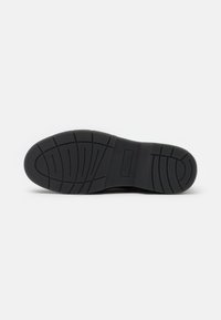 Black rubber shoe sole with textured grip patterns and flex grooves. Rounded toe and slight curvature at heel, minimal design details.