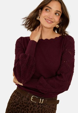 Burgundy knit sweater with scalloped neckline and textured balloon sleeves; paired with brown leopard-print pants and a belt.