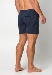 Marinblå badbyxor tillverkade av lättviktigt tyg. Elastisk midja med en bakficka och små ögla-detaljer. Minimalistisk design.