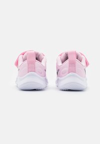 Zapatillas deportivas rosas con una parte superior lisa y una suela de goma blanca. Cuentan con una pestaña en el talón y un logo plateado en el costado.