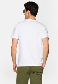 Biała bawełniana koszulka z okrągłym dekoltem, krótkimi rękawami i gładkim tyłem, z minimalnym logo w okolicy dekoltu.