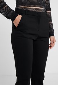 Svarta skräddarsydda byxor med en slät, matt yta, som har en platt framsida och sidofickor. Tillverkade av stretchigt tyg för komfort.