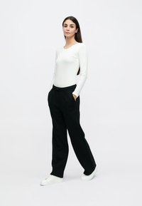 Λευκό μακρυμάνικο τοπ συνδυασμένο με μαύρο παντελόνι χαλαρής εφαρμογής και λευκά αθλητικά παπούτσια. Το παντελόνι έχει τσέπες και ρυθμιζόμενη μέση με κορδόνι.