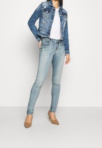 Ljusblå denimjacka med en figursydd design, två bröstfickor och knäppdetaljer, tillsammans med ljus tvättade skinny jeans och beige klackskor.